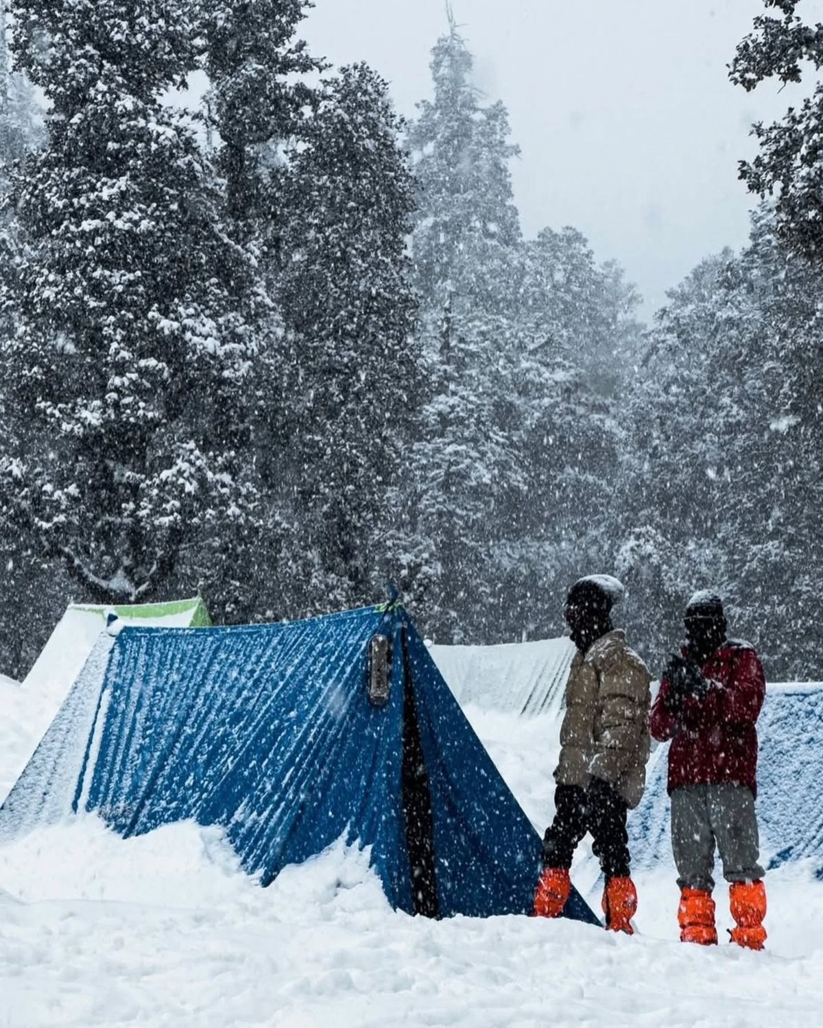 Two trekkers beside a tent in falling snow