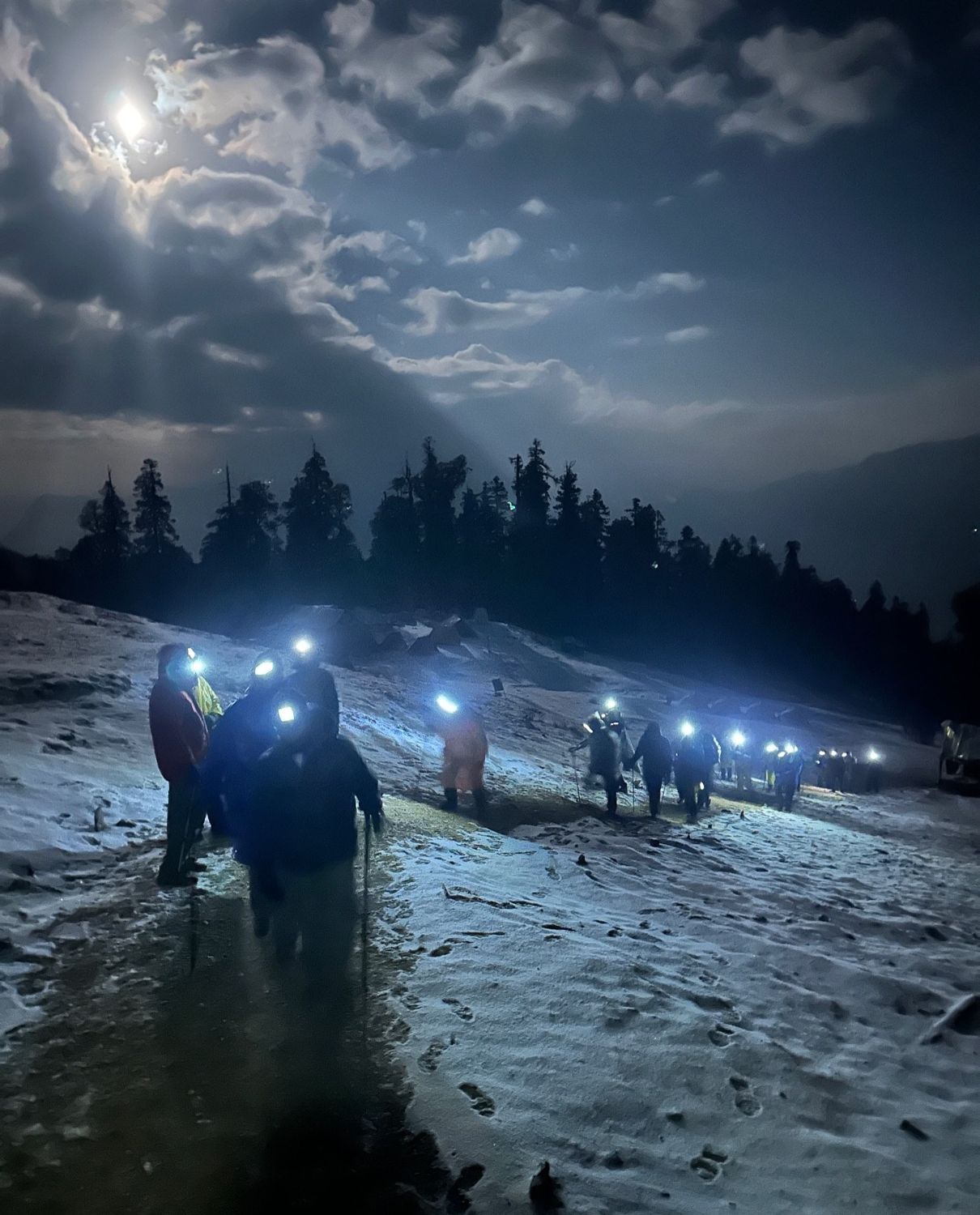 Trekkers with head torches on a snowy trail at night