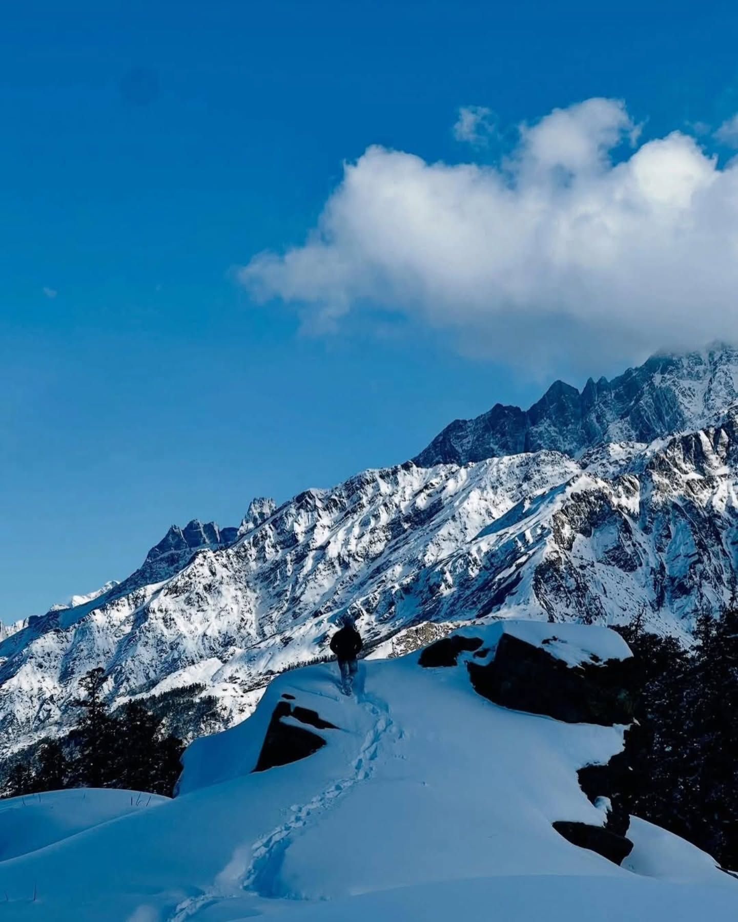 A trekker on a snow ridge below the Kedarkantha range under a blue sky