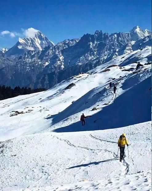 A trekker on snow with peaks behind
