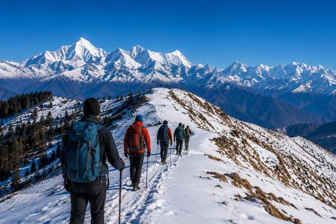 Trekkers on a snow ridge facing a wall of peaks