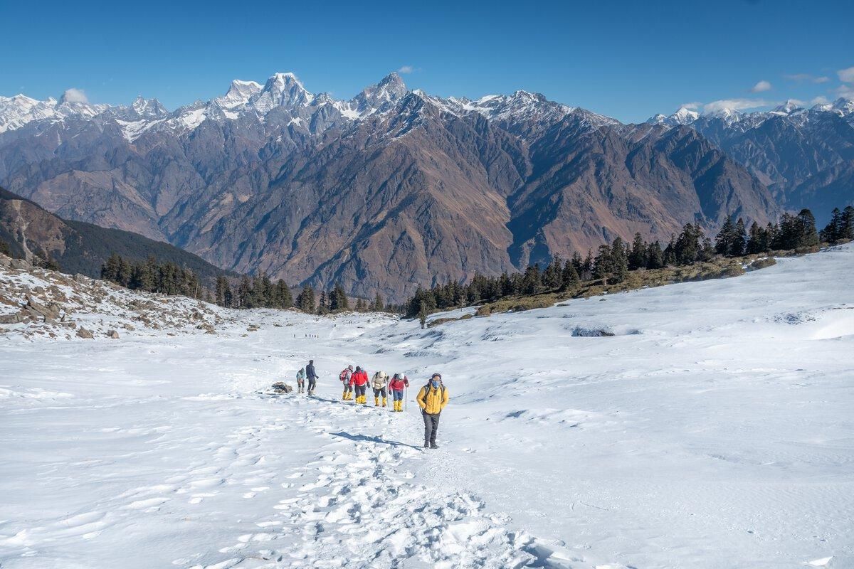 Trekkers crossing a snow meadow with peaks behind
