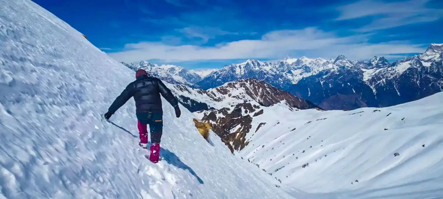 A trekker on a snowy ridge with the range behind