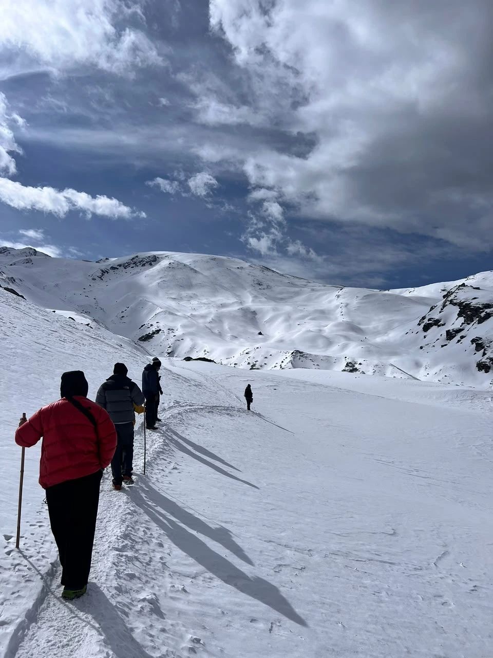 Trekkers walking across snow under a dramatic sky