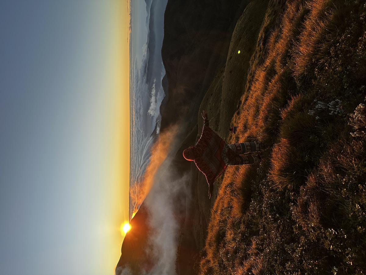 A figure with arms raised at sunrise above the clouds