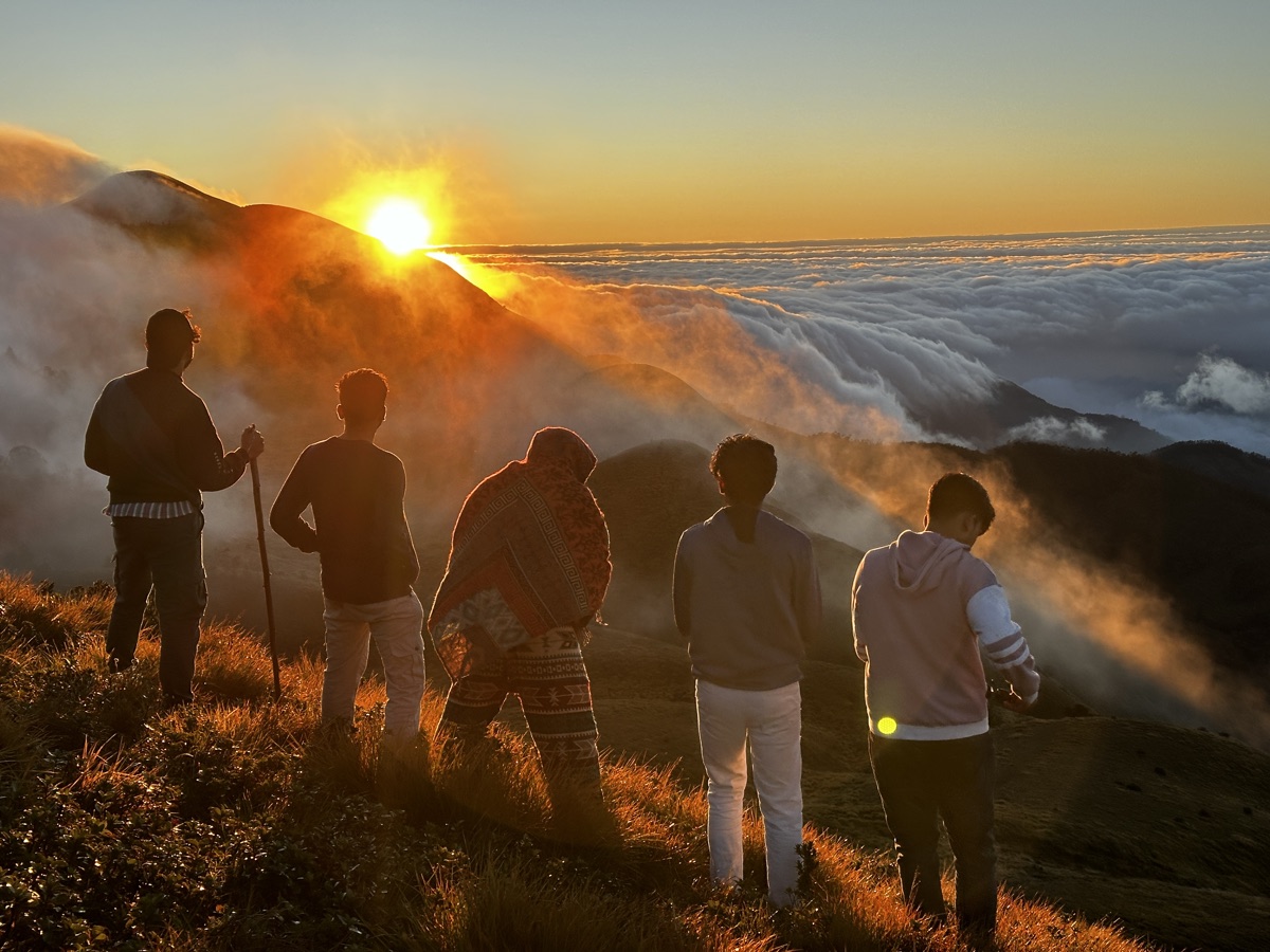 Sunbeams breaking over the ridge as trekkers watch the sunrise
